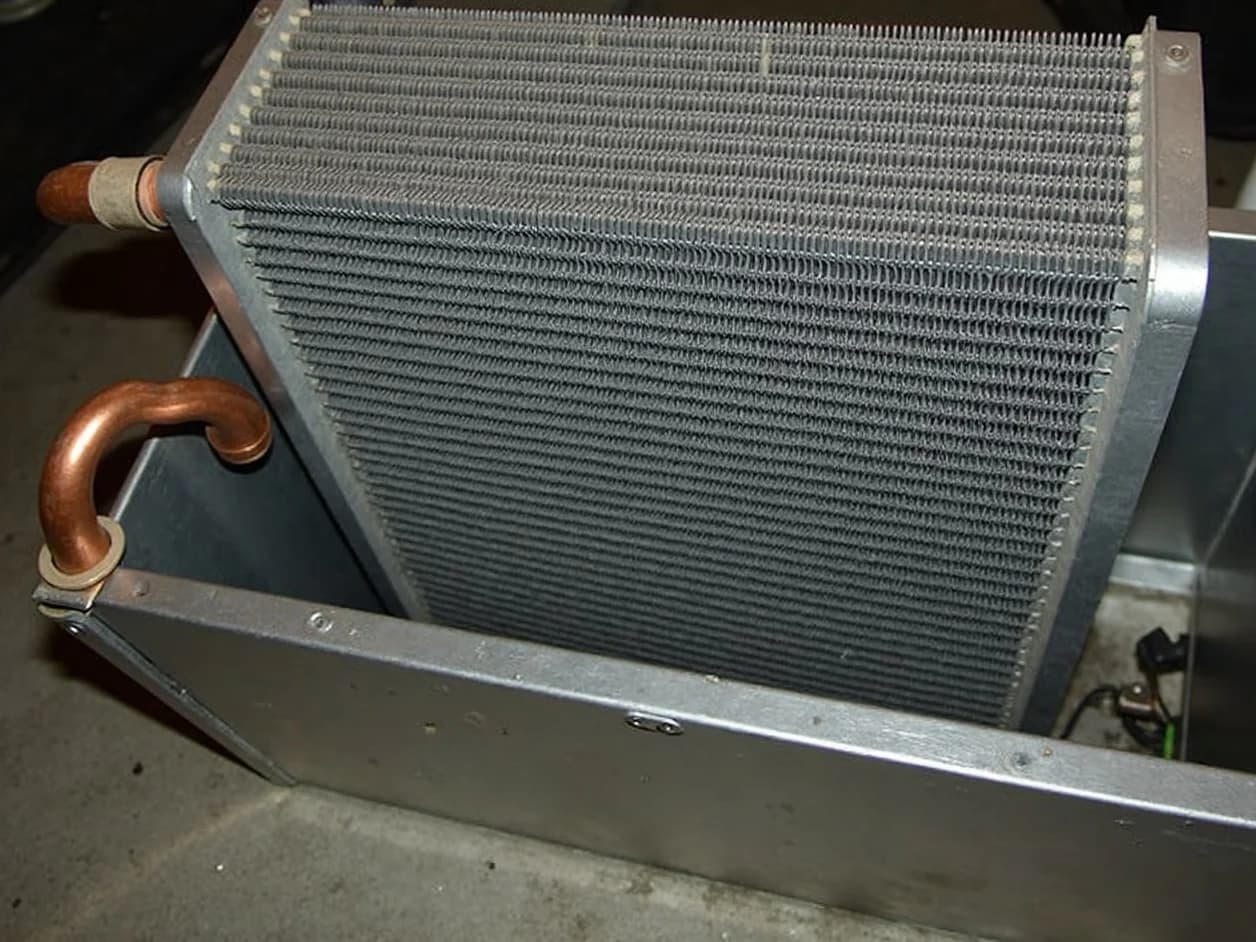 Indoor evaporator coil in an opened sheet-metal plenum above a residential furnace